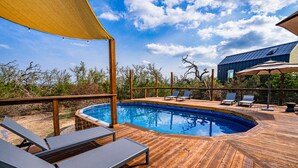 Una terraza de madera con piscina, sillas de descanso y una zona cubierta con toldo amarillo.