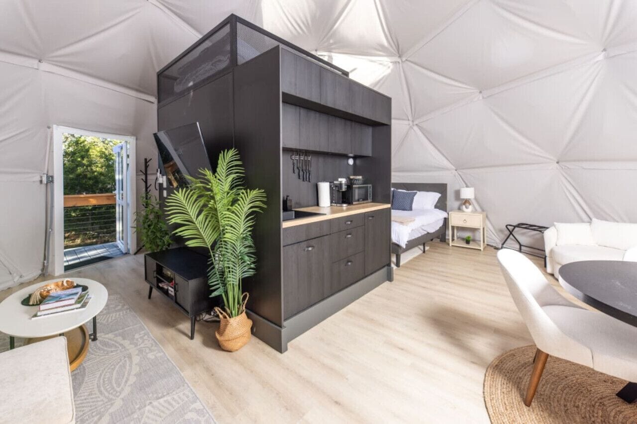 Un hébergement compact et moderne, aménagé comme une tente, comprenant un coin cuisine, un lit et un espace salon.