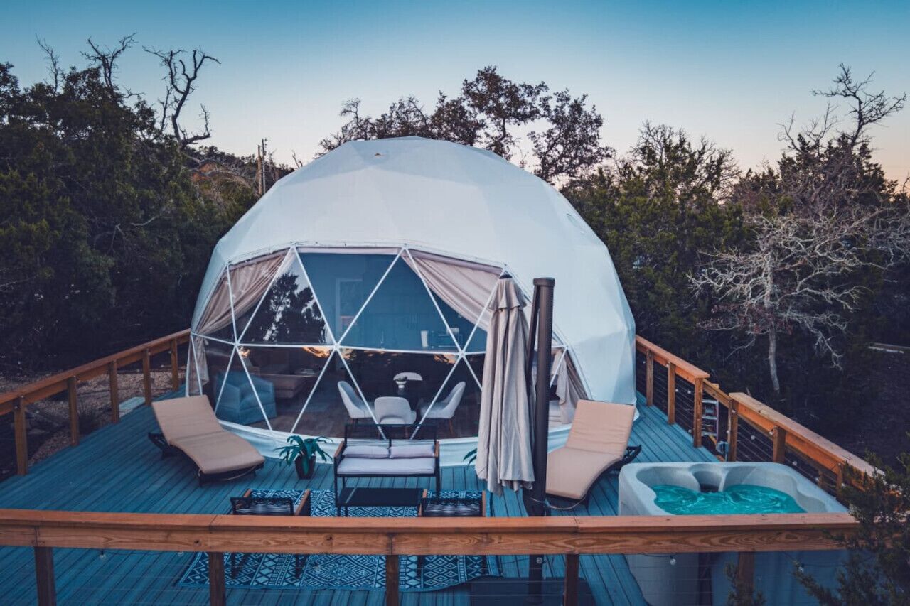 A geodesic dome structure with a deck, lounge chairs, and a hot tub.