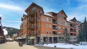 A multi-story hotel with balconies, a ski slope in the background, and a snowy ground. - Studio Condo w/ Fireplace & Pool | Near Gondola! (Keystone)