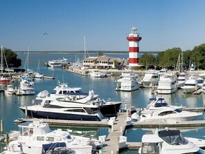 Marina com vários barcos atracados, um farol imponente e um edifício com fachada branca.