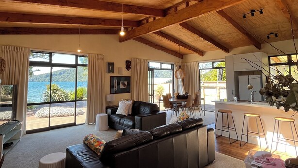 A spacious living area with a large black leather sofa, a dining table, and a kitchen area. - Lake Rotoiti - Absolute Lakefront (Rotoiti Forest)