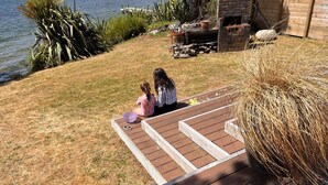 A wooden deck with a fire pit and a brick building in the background. - Lake Rotoiti - Absolute Lakefront (Rotoiti Forest)