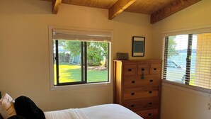 A bedroom with a bed, a dresser, and two windows. - Lake Rotoiti - Absolute Lakefront (Rotoiti Forest)