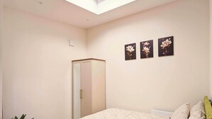 Un dormitorio con cama, armario, tragaluz y tres cuadros florales en la pared.