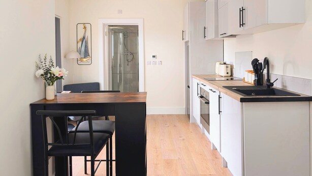 Una cocina moderna con armarios blancos, una encimera de madera y una silla negra en la mesa de comedor.