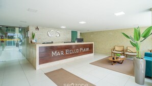 A reception area with a wooden reception desk labeled "MAR BELLO PLAZA," a seating area with chairs and a coffee table, and a large potted plant. - Your Complete Stay With a Rooftop Pool, 40m From the Beach in Cabedelo Cmzs (Cabedelo)