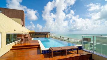 Piscina en la azotea con vista al océano, terraza de madera y mobiliario exterior.
