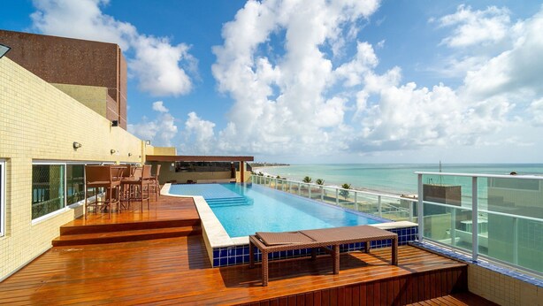 A rooftop pool with a view of the ocean, wooden deck, and outdoor seating. - Your Complete Stay With a Rooftop Pool, 40m From the Beach in Cabedelo Cmzs (Cabedelo)