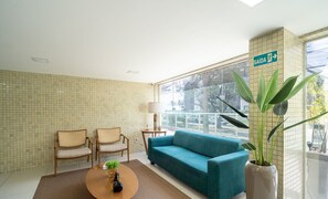 A modern room with a teal sofa, two wicker chairs, a coffee table with a plant, and a large window with a view of the outside. - Your Complete Stay With a Rooftop Pool, 40m From the Beach in Cabedelo Cmzs (Cabedelo)
