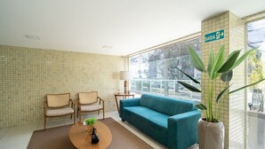 A modern room with a teal sofa, two wicker chairs, a coffee table with a plant, and a large window with a view of the outside. - Your Complete Stay With a Rooftop Pool, 40m From the Beach in Cabedelo Cmzs (Cabedelo)