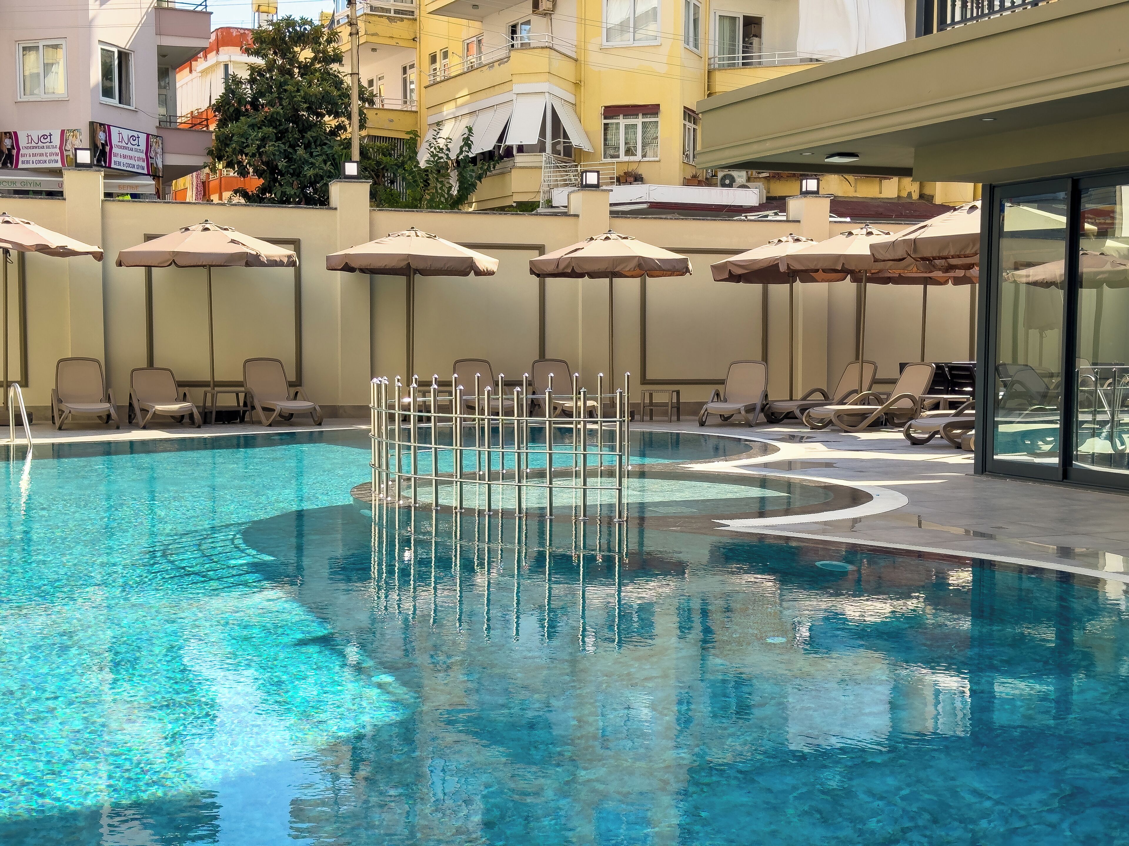 Piscina com espreguiçadeiras e guarda-sóis, cercada por edifícios.
