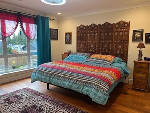 A bedroom with a large bed, a wooden headboard, a window with curtains, a bedside table, and a nightstand. - Warm Family Retreat in the Heart of Coquitlam (Coquitlam)