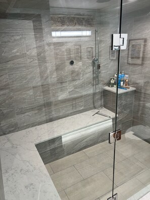 A modern shower with a glass door, marble tiles, and a small shelf with toiletries. - Warm Family Retreat in the Heart of Coquitlam (Coquitlam)