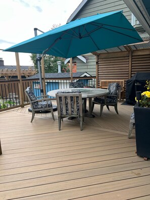 A wooden deck with a round table and four chairs, an umbrella, and a grill. - Warm Family Retreat in the Heart of Coquitlam (Coquitlam)