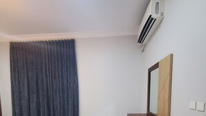 A room with a white tiled floor, a dark curtain, a wooden cabinet, and an air conditioning unit mounted on the wall. - Rehana Hotel (Khamis Mushait)
