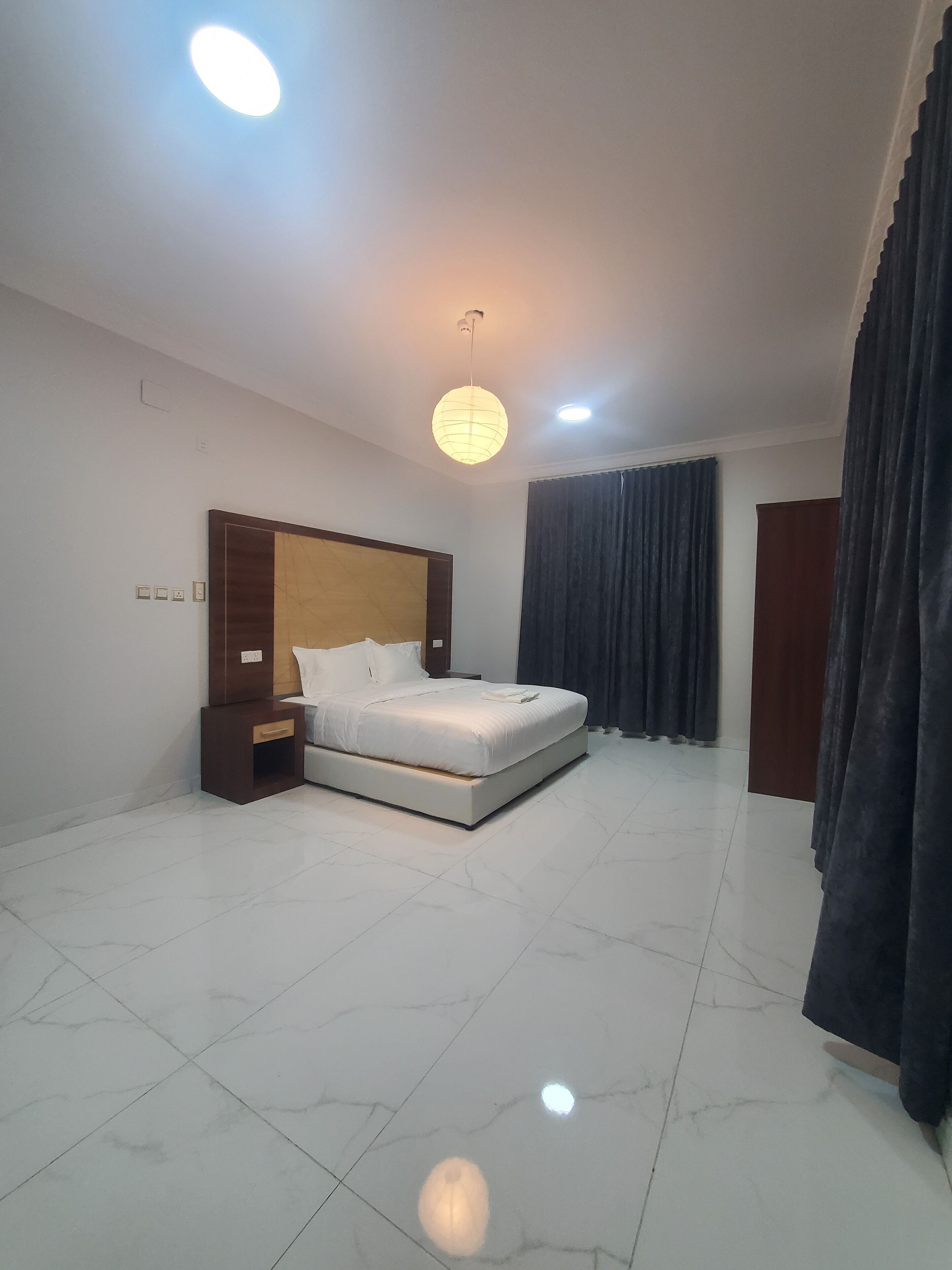 Habitación de hotel con una cama grande, una mesita de noche, una lámpara colgante y una cortina oscura.