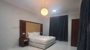 A hotel room with a large bed, a bedside table, a nightstand, a hanging light fixture, and a dark curtain. - Rehana Hotel (Khamis Mushait)