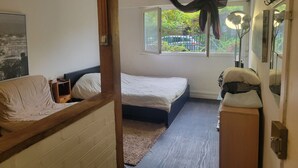Un dormitorio con cama, ventana con cortinas, mesita de noche y espejo.
