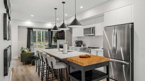 A modern kitchen with a central island, stainless steel appliances, and pendant lighting. - Chalet Grande Ourse | Slope-Side | Private Hot Tub (Panorama)
