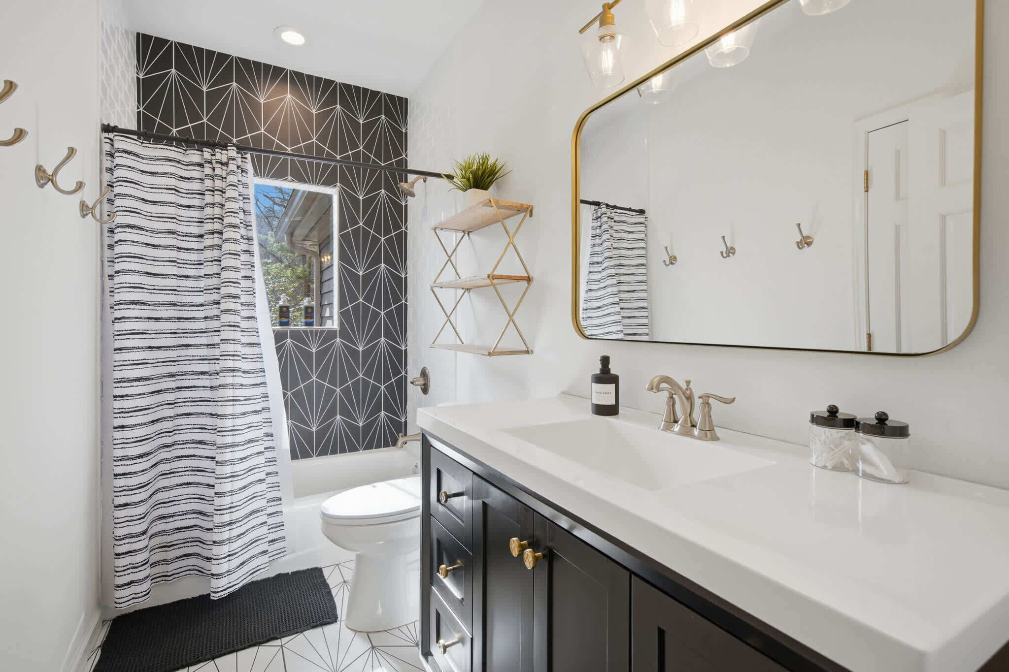 Um banheiro moderno com pia branca, cortina de chuveiro listrada em preto e branco, azulejos geométricos e um espelho grande.