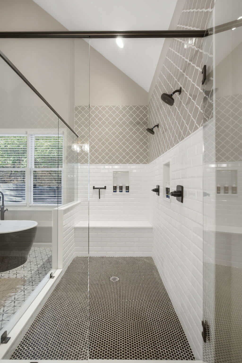 A modern bathroom with a glass-enclosed shower, a freestanding bathtub, and a large window with blinds.