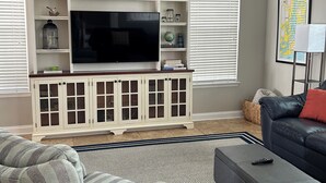 A living room with a TV on a white cabinet, a ceiling fan, and a map on the wall. - Pond View near Old Town Bluffton (Bluffton)
