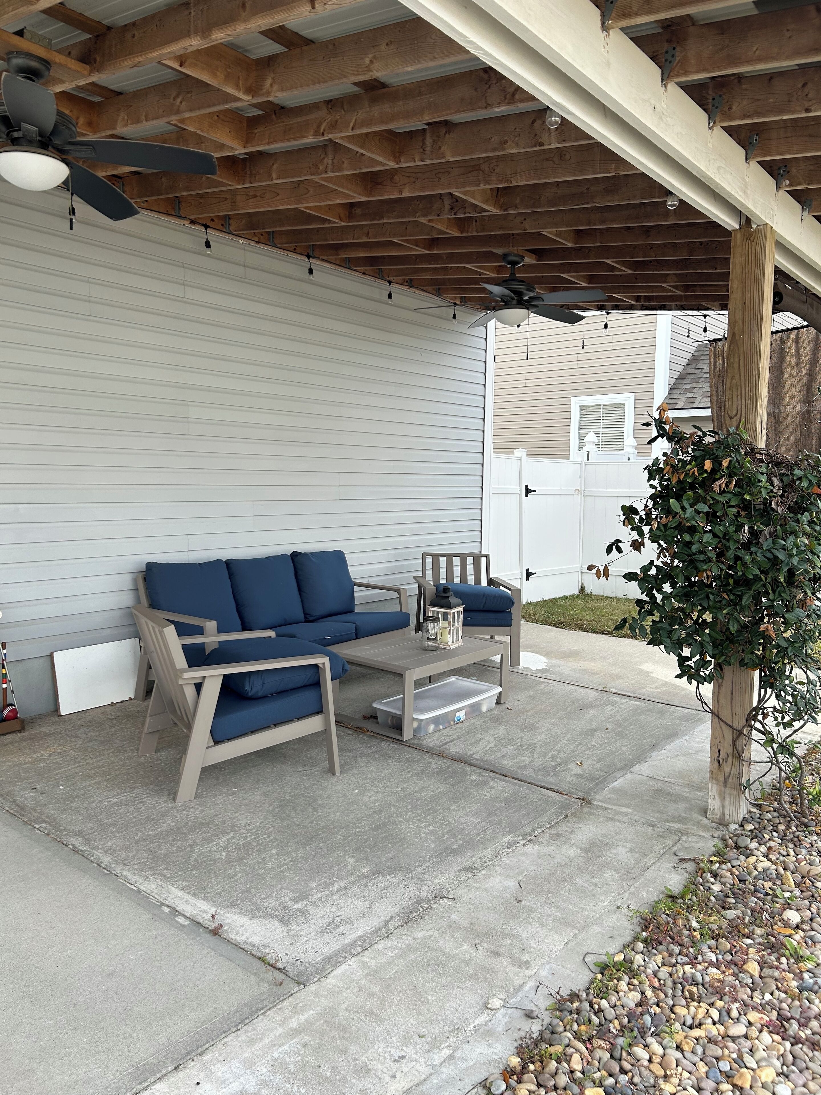 Un'area patio coperta con soffitto in legno, un divano beige, un tavolino e una pianta in vaso.