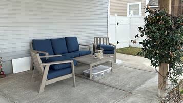 Un'area patio coperta con soffitto in legno, un divano beige, un tavolino e una pianta in vaso.
