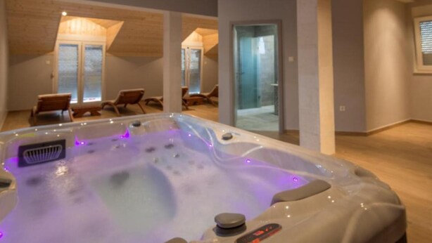 A modern spa room with a hot tub, wooden ceiling, and seating area. - Six Bedroom Holiday House With Pool (Benkovac)