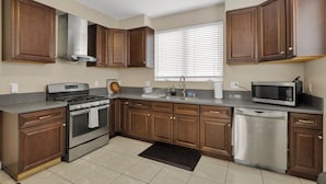 A kitchen with wooden cabinets, stainless steel appliances, a dishwasher, and a window with blinds. - HUGE 3BD 2.5BA • 2,118 Sq Ft • Sleeps 11 • KING BD (San Gabriel)