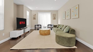 A living room with a flat-screen TV, a round wooden coffee table, a green sofa, and a large beige rug. - HUGE 3BD 2.5BA • 2,118 Sq Ft • Sleeps 11 • KING BD (San Gabriel)