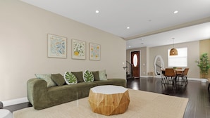 A modern living room with a green sofa, a round wooden coffee table, and three framed artworks on the wall. - HUGE 3BD 2.5BA • 2,118 Sq Ft • Sleeps 11 • KING BD (San Gabriel)