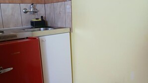 Eine kleine Küche mit Spüle, einem Kühlschrank und einer roten Mülltonne.