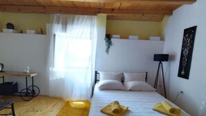 Ein Schlafzimmer mit einem Bett, einem Schreibtisch, einem Stuhl, einem Fenster mit Vorhängen und einer Wandpflanze.