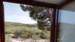 Ein Zimmer mit großem Fenster und Blick auf eine angelegte Außenanlage mit Bäumen und einer Terrasse.