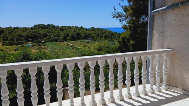 A balcony with white balustrades overlooking a lush green landscape and a clear blue sky. - Apartmani Green Oasis - One Bedroom Apartment with Terrace and Sea View (Vis)