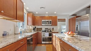 A modern kitchen with wooden cabinets, stainless steel appliances, granite countertops, and a patterned rug. - Water Views, Dog Friendly, Fire Pit in Brewster (Brewster)