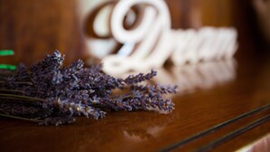 Una superficie de madera con un fondo desenfocado, un ramillete de flores de lavanda y un objeto blanco con un diseño espiral.