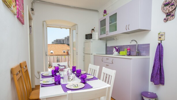 Una cocina compacta con microondas, lavabo y armarios. Un comedor contiguo presenta una mesa con sillas y manteles individuales morados.