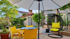 Un patio al aire libre con sillas amarillas, una mesa redonda y un sillón colgante con cojines amarillos.