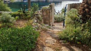 Un sentier de pierres mène à une construction rustique en pierre, d’où l’on peut admirer un lac paisible et des bateaux.