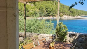 Une table en bois sur laquelle est posé un vase de fleurs, un mur de pierre et une vue sur un lac où l’on aperçoit des bateaux.