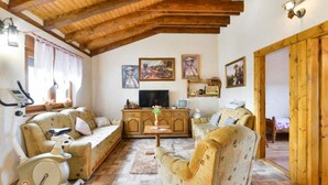 A cozy living room with wooden beams, a sofa, a TV, and a bike. - Holiday House Šimun - Three bedroom Holiday house with pool (Stankovci)