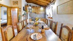 A dining area with a wooden table set for six, surrounded by chairs. A kitchen with wooden cabinets and a tiled backsplash is visible in the background. - Holiday House Šimun - Three bedroom Holiday house with pool (Stankovci)
