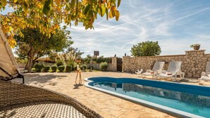 A swimming pool with lounge chairs and a wicker chair, surrounded by stone walls and vegetation. - Holiday House Šimun - Three bedroom Holiday house with pool (Stankovci)