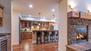 A spacious kitchen with wooden cabinets, a central island with bar stools, a stone fireplace, and recessed ceiling lights. - 4 BR / 3.5 BA Home Near Downtown Truckee & Skiing! (Truckee)