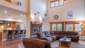 A spacious living area with a large brown leather sectional sofa, a stone fireplace, and a kitchen with wooden cabinets and bar stools. - 4 BR / 3.5 BA Home Near Downtown Truckee & Skiing! (Truckee)