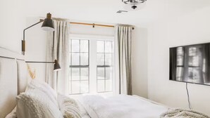 A bedroom with a bed, a desk lamp, a TV, and a window with curtains. - Cozy Historical Home, Walk to Downtown Edmond (Edmond)