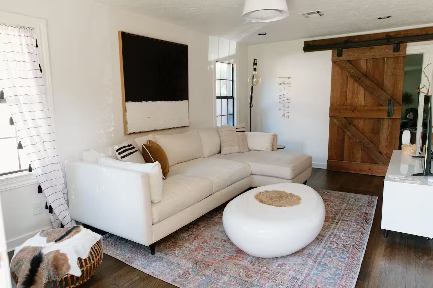 Un salon moderne avec un canapé d’angle, un pouf rond, un tapis à motifs et une grande porte en bois.